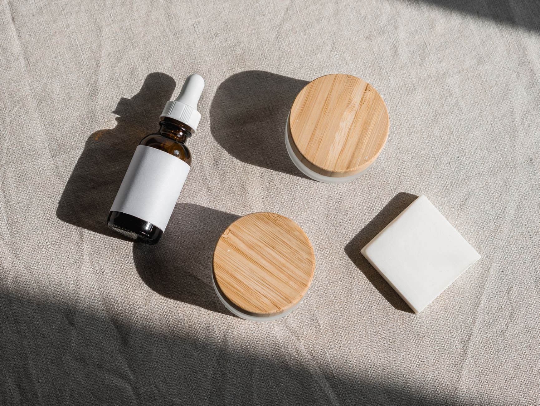 Flat lay of natural skincare products with wooden lids on linen fabric background